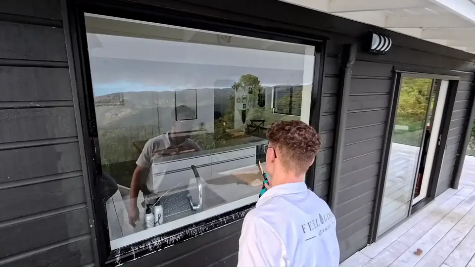 Kilian cleaning a large window on a dark weatherboard home